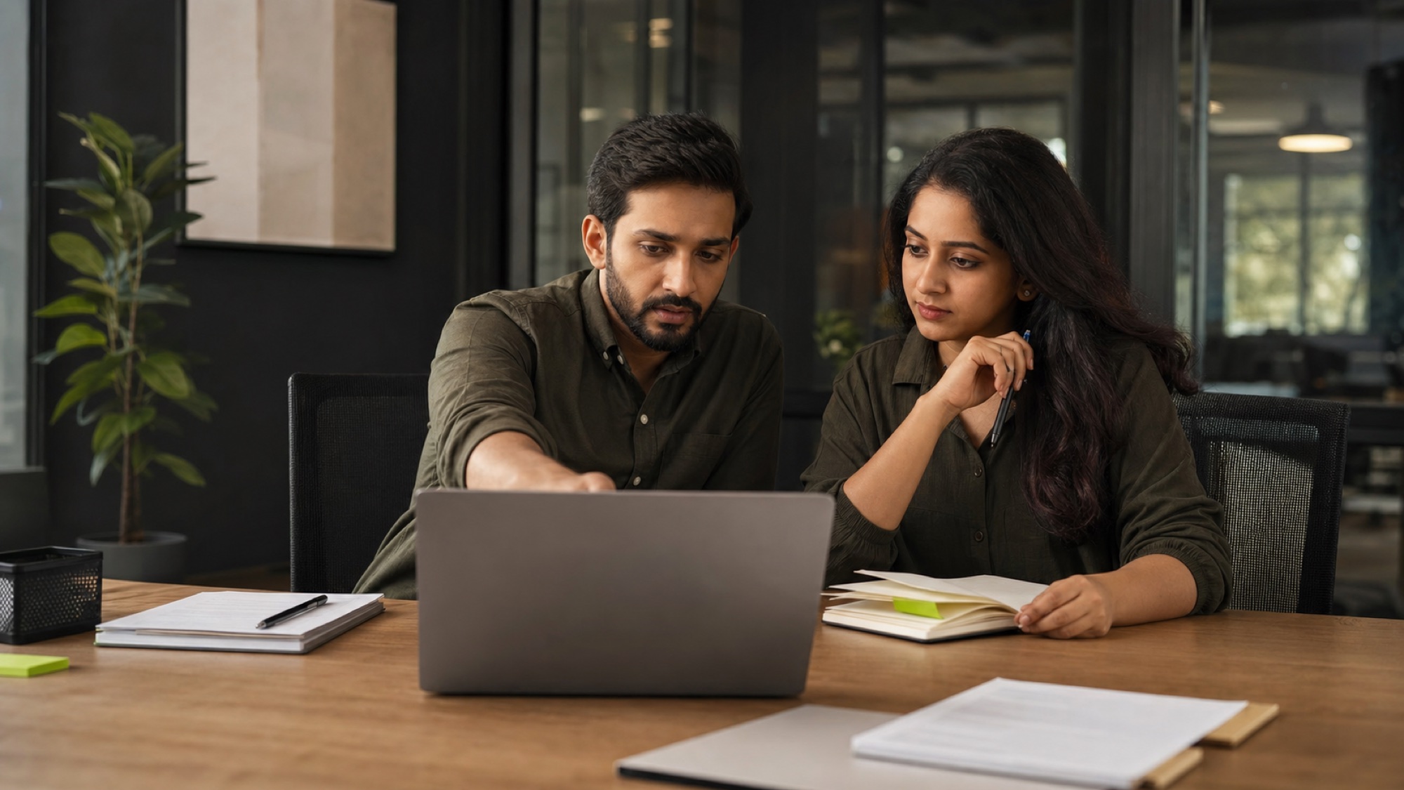 Two operations professionals compare customer work together at a laptop.